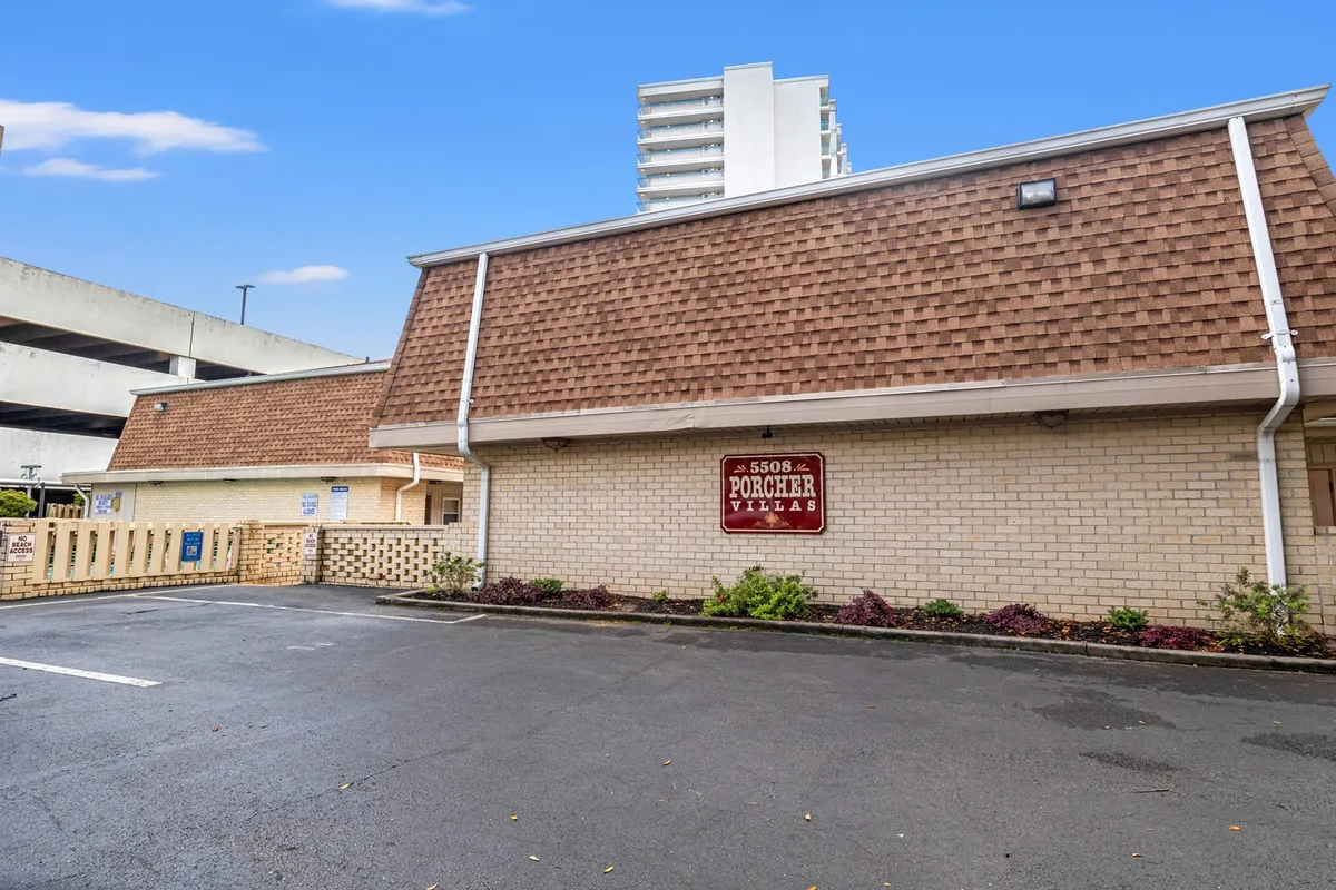 This image displays the exterior of Porcher Villas, highlighting the inviting building facade with clear signage, well-maintained landscaping, and a relaxed parking area. The scene conveys a sense of community and serves as a visual introduction to the property as a comfortable home base for snowbirds.