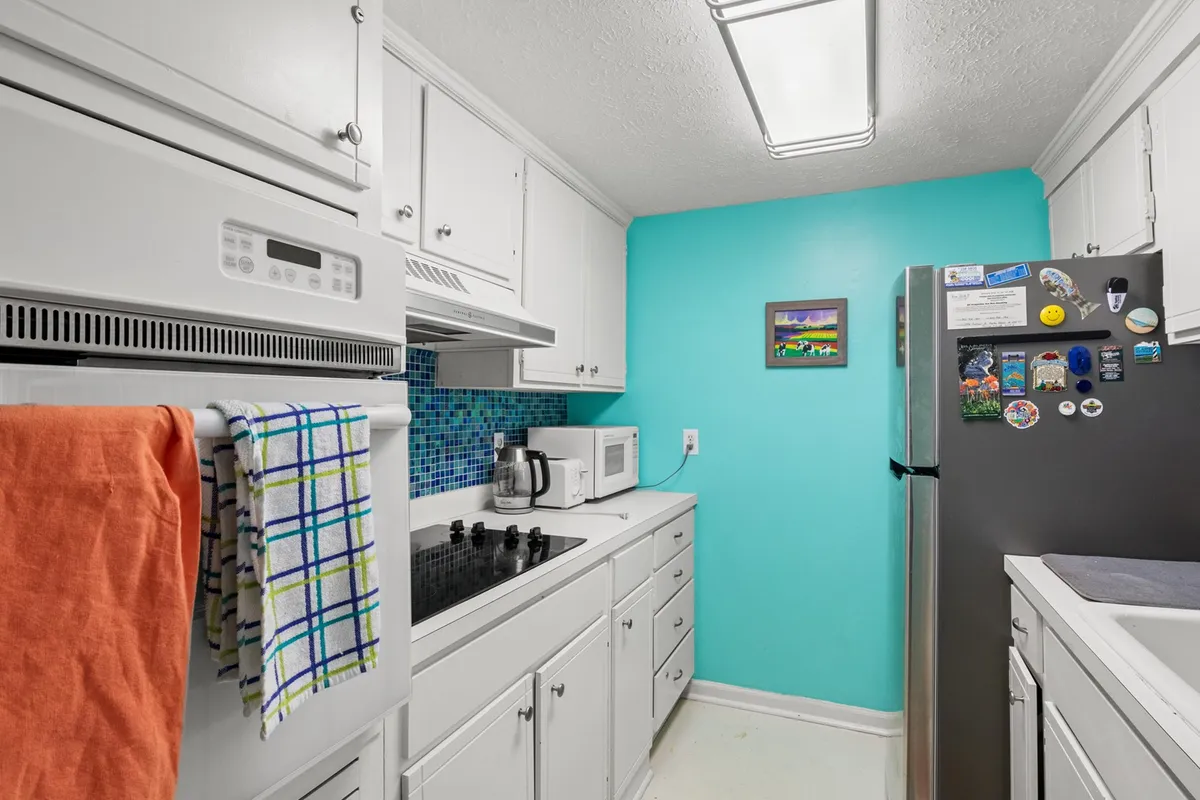A bright, cheerful kitchen with a turquoise accent wall, colorful backsplash, stainless steel refrigerator, and vibrant artwork. The space is modern, fully equipped, and designed for family cooking and gatherings.