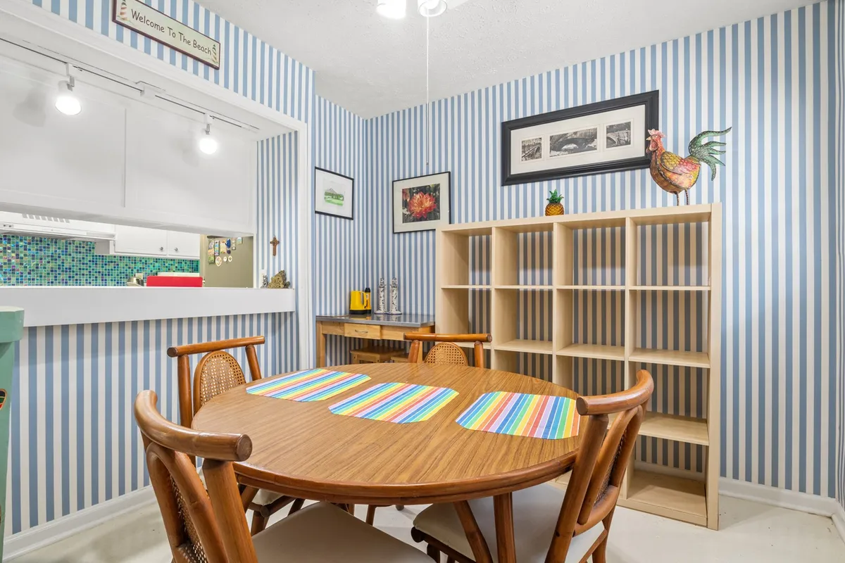 A round wooden dining table set with colorful striped placemats sits adjacent to open shelving and decorative wall art. The area feels playful yet intimate—a setting crafted for family meals, casual gatherings or game nights.